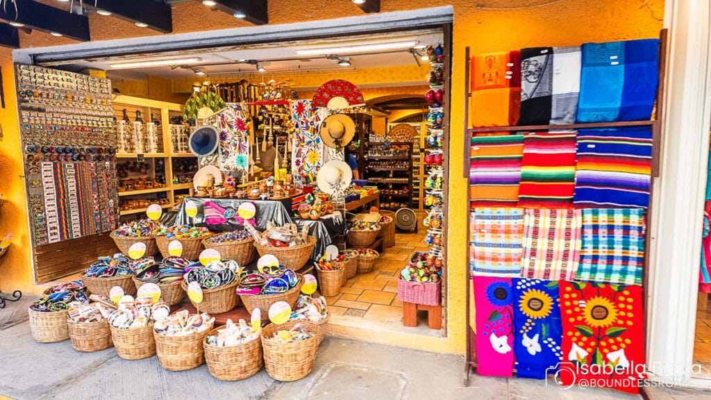 Colorful market stall displaying vibrant textiles, hats, and crafts in woven baskets. Brightly decorated entrance with a rich assortment of traditional handmade goods.
